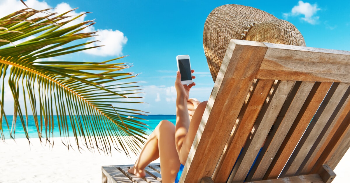 Eine Frau liegt mit ihrem Handy am Strand.