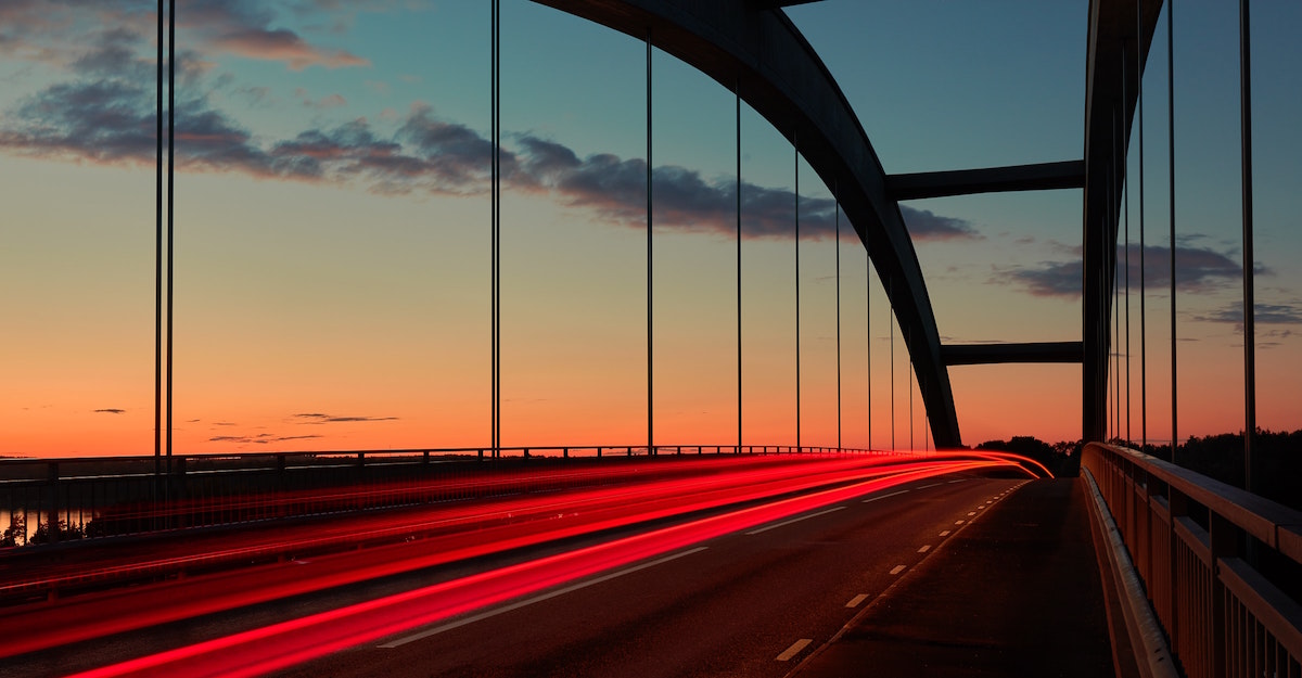 Abendliche Szene auf einer Brücke, im Hintergrund Abendrot, mit Langzeitbelichtung der Fahrzeuglichter