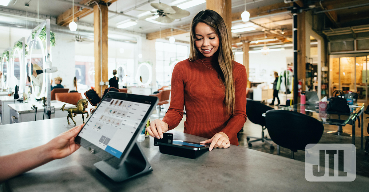 Eine junge Frau bezahl an einer Ladentheke mit ihrer Karte. Auf der Ladentheke steht eine elektronische Kasse mit Touchscreen.