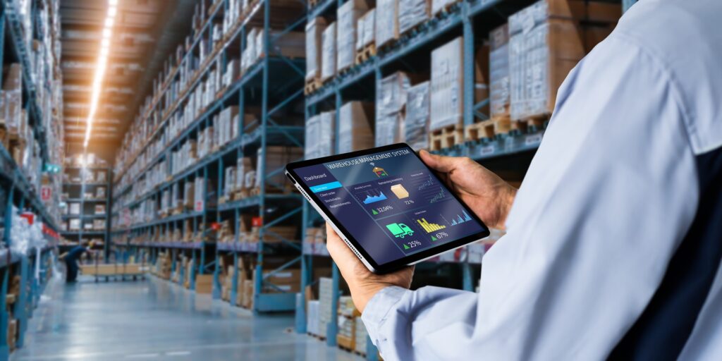 Mann mit einem Tablet, auf dem das Dashboard eines Warehouse Management Systems zu sehen ist, in einer Lagerhalle